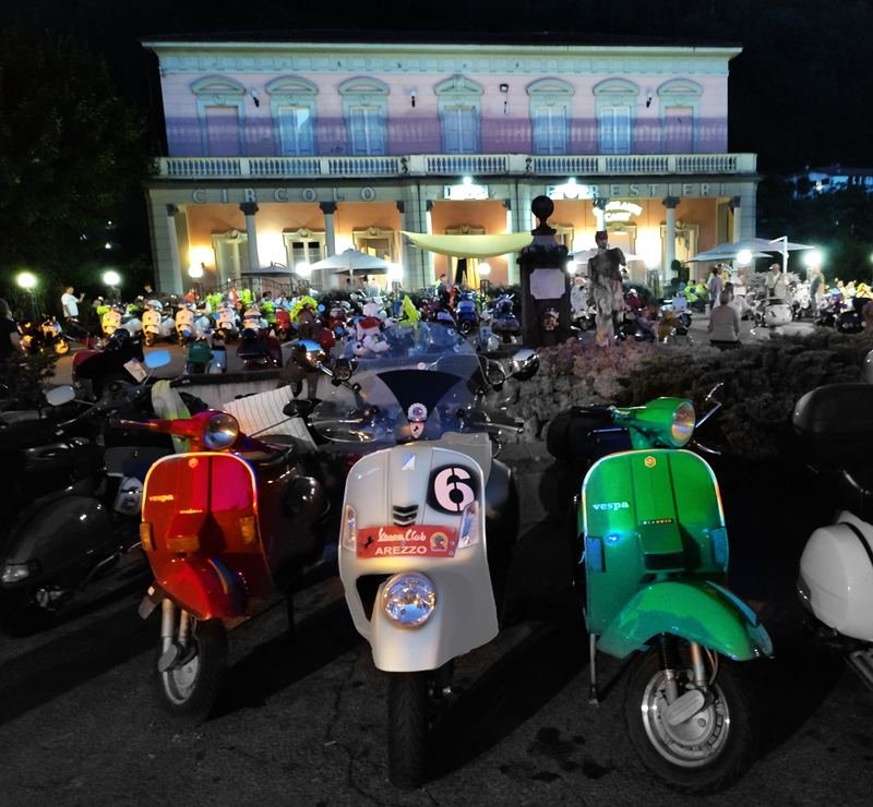 Vespa scooters lined up at night in front of the floodlit Circolo dei Forestieri