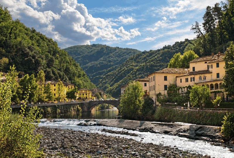The stone bridge at Ponte a Serraglio over the Lima river, with ochre riverside houses and green wooded hills